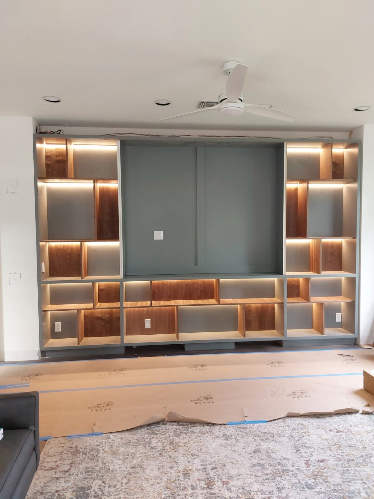 Custom built-in shelving wall with walnut interiors and concealed LED strip lighting, under construction