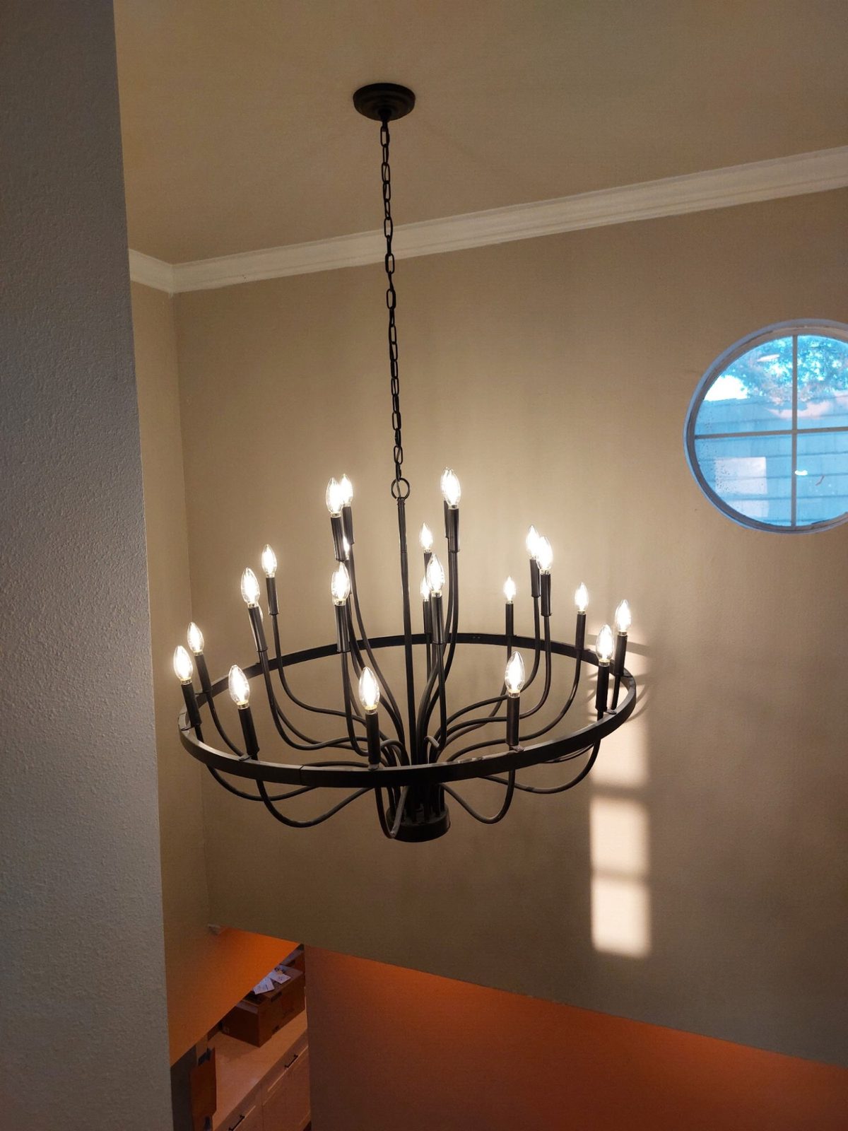 Large black iron candelabra chandelier installed in a two-storey entry with a round window