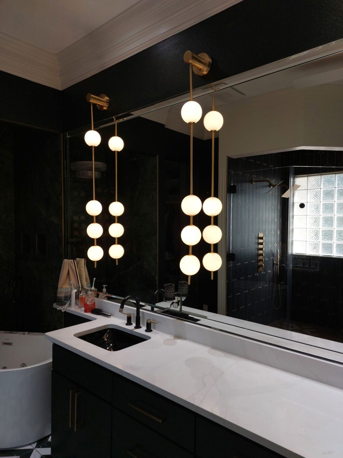 Brass globe pendant lights installed over a white marble double vanity in a dark primary bathroom